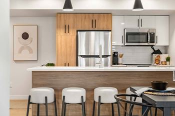 A modern kitchen with a wooden island and white stools.